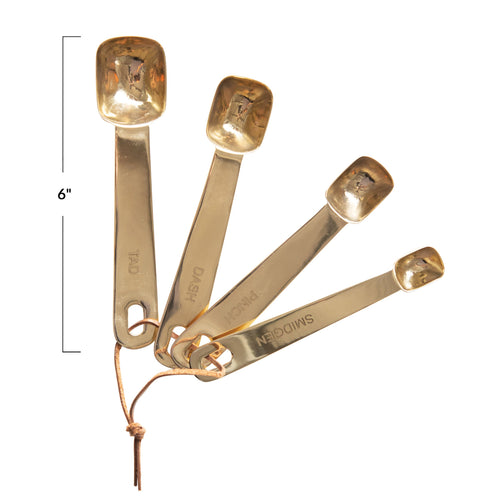 A set of four stainless steel square measuring spoons with brass finish and leather ties.