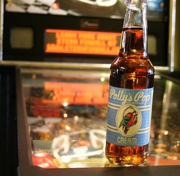 A bottle of cream flavored Polly's Pop on a pinball machine.