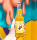 A person holding a bottle of pineapple Polly's Pop against a blurred colorful background.