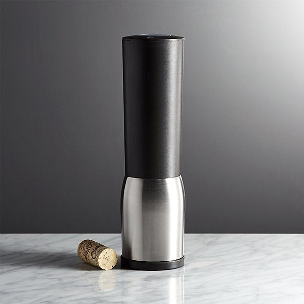 An electric corkscrew in black and silver with a cork next to it on a marble surface and gray background.