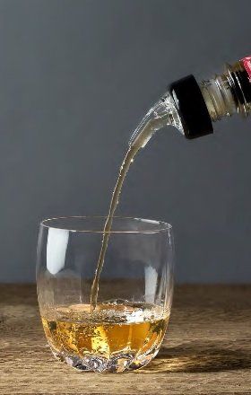 A glass with liquid poured into it via a measured pourer.