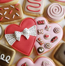 A collection of cookies with a double heart cookie in the center decorated to look like a Valentine's Day box of chocolates.