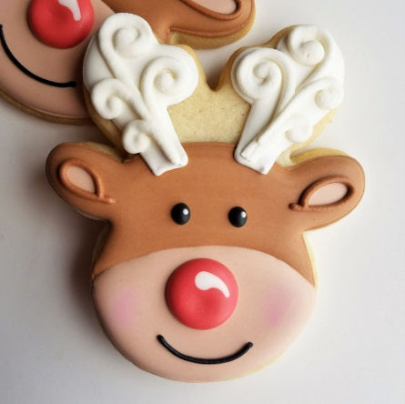 A cookie in the shape of a reindeer head with white antlers and a red nose