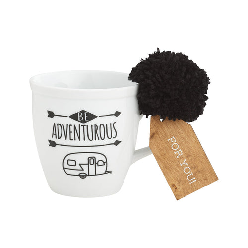 A white porcelain mug with black text and a black camper illustration, accompanied by a black pom-pom and a wooden gift tag with 'FOR YOU' printed on it.