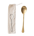 A gold-colored brass spoon placed next to a beige printed drawstring bag with a drawing of a spoon on it.