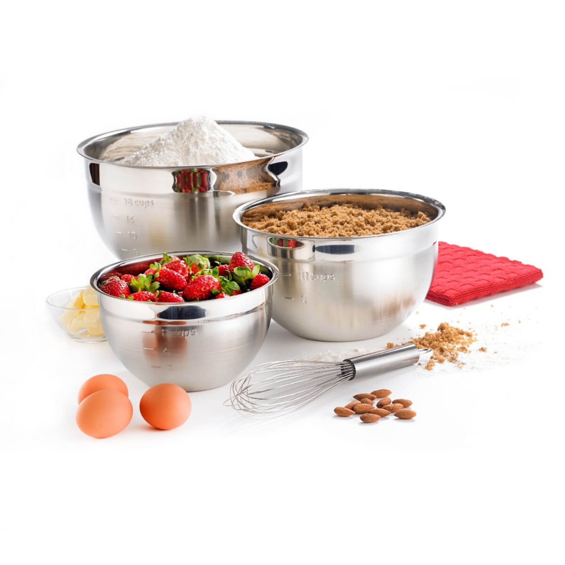 A set of three stainless steel mixing bowls of different sizes with a whisk in front and ingredients around them, displayed on a white background.