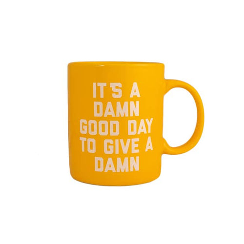 A yellow ceramic mug with black text that reads 'It's a DAMN good day to give a DAMN'.