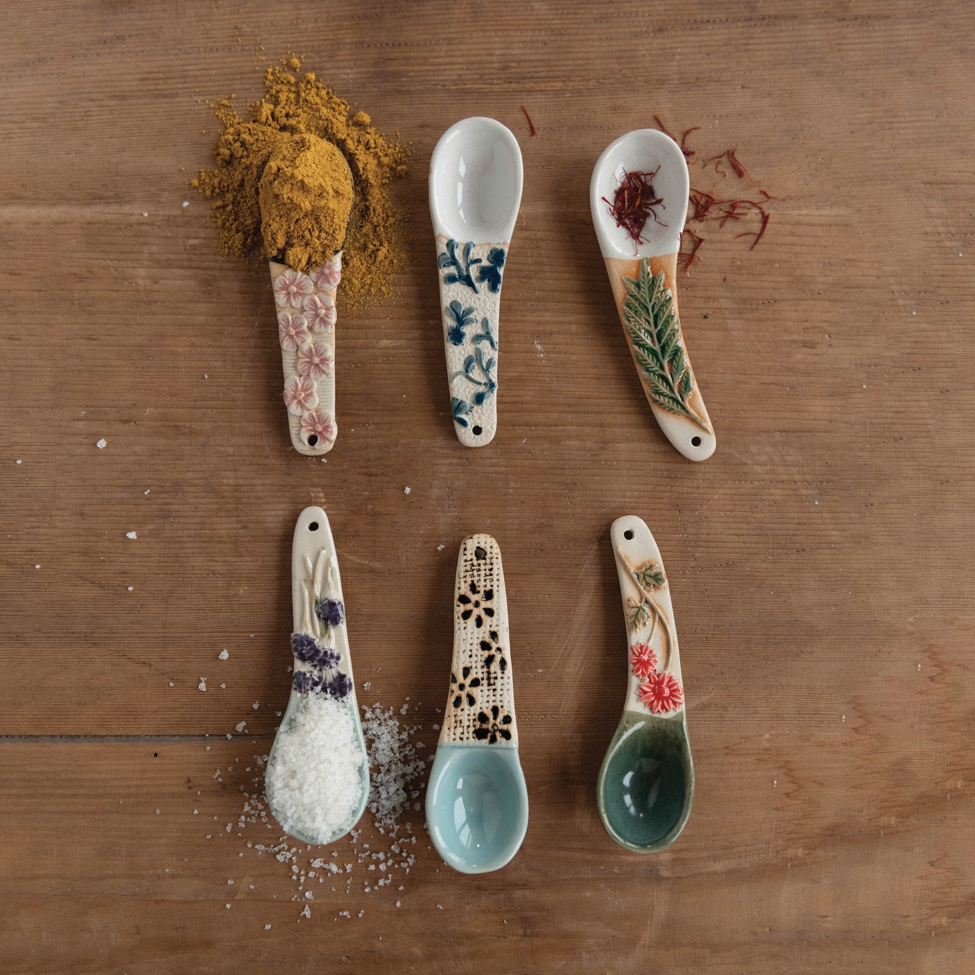6 hand painted spoons on a wooden surface, some with spices in them.