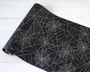 A roll of black table runner with a spider web pattern.