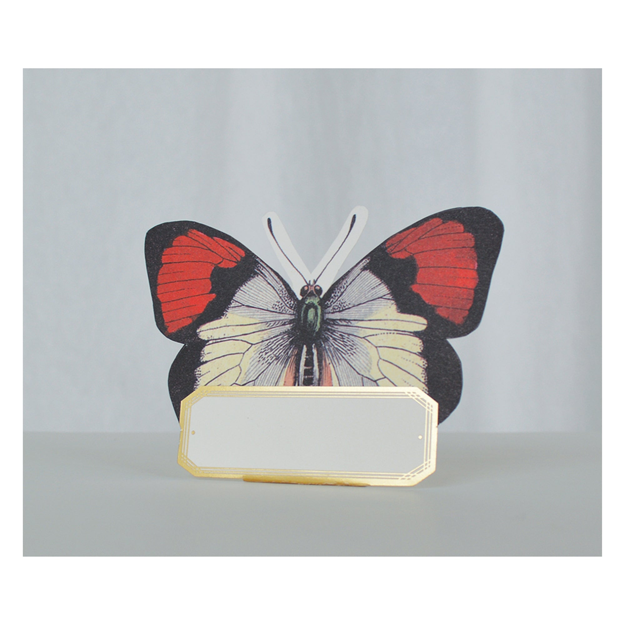 A die cut butterfly-shaped place card with gold foil details, red and black coloring, and a blank space for writing.