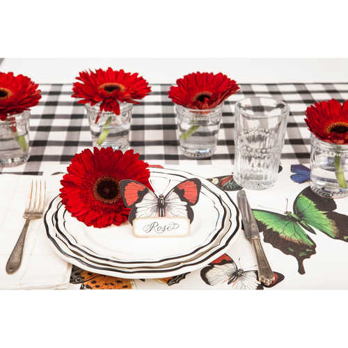 A place setting featuring black plaid table runner, butterfly placemats, plates, glasses with flowers, and a butterfly place card.