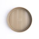 A round, beige-colored Cuisipro baking pan with a textured wave bottom, displayed against a white background.