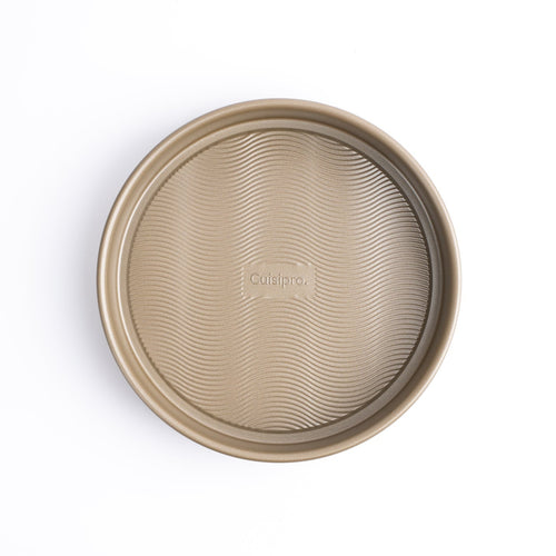 A round, beige-colored Cuisipro baking pan with a textured wave bottom, displayed against a white background.