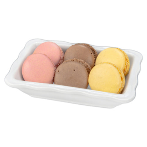 A small scalloped dish with six macaron cookies in different colors on a white surface.