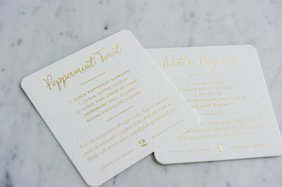 Recipes for drinks on white coasters lying on a marble background.